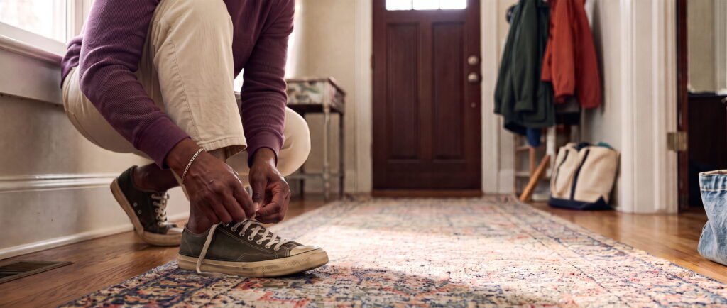 A woman crouched in her hallway, lacing up her trainers by the front door