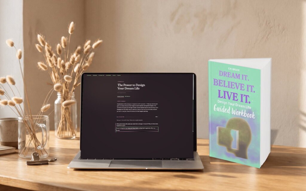 The Dream Life Workbook open on a laptop, beside the printed guided workbook, on a sunlit desk